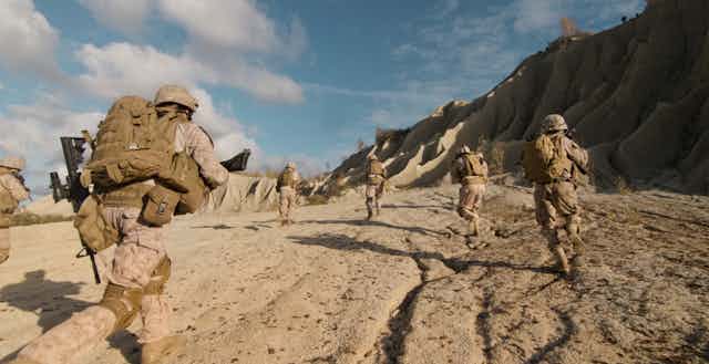 Des soldats armés courent dans un désert entouré de montagnes.