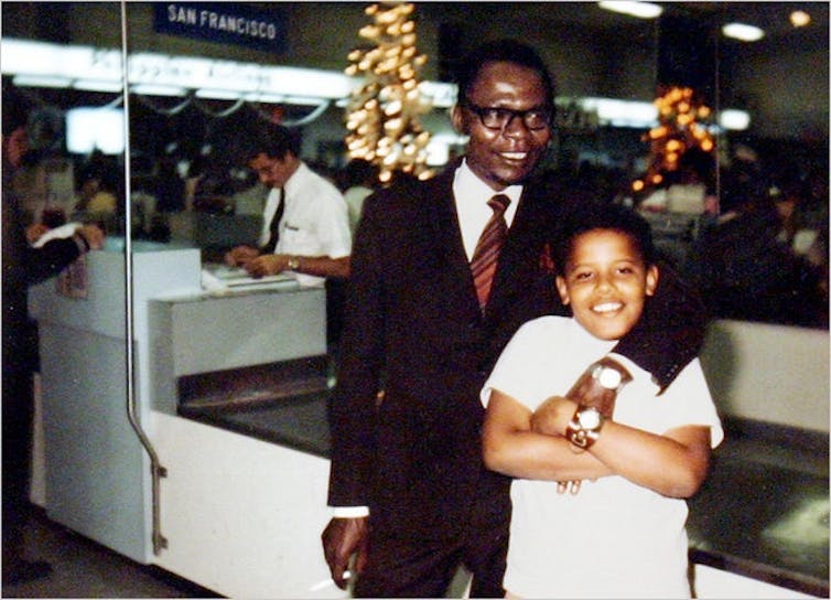 A man in a suit and tie poses with his arm around a young boy