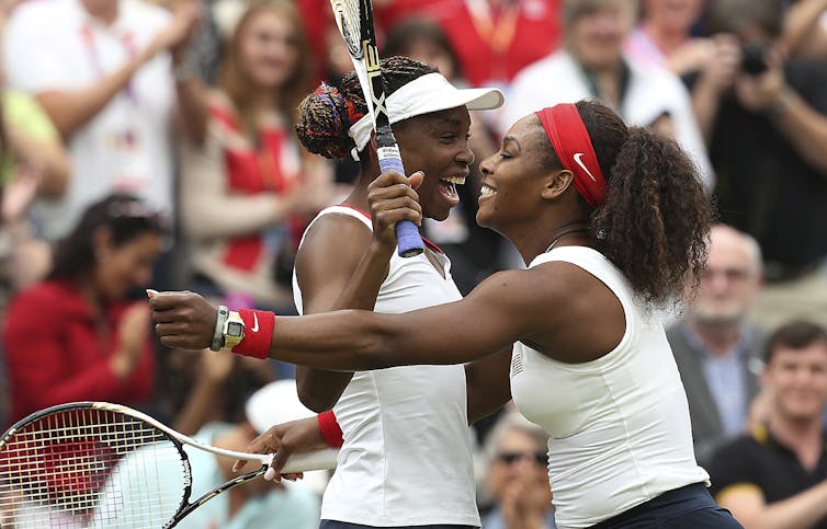 Serena and Venus Williams laugh on the tennis court.