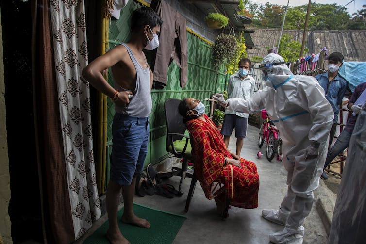 A health-care worker dressed in PPE takes a nasal swab from a woman in India.