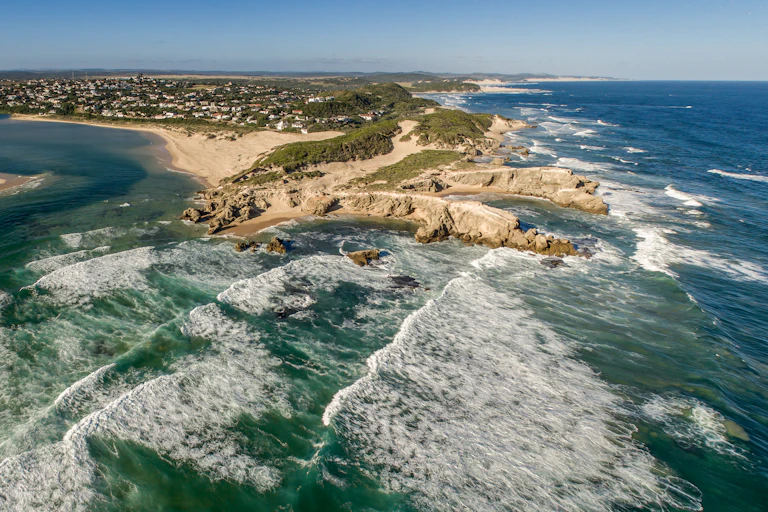 An aerial view of a rocky cove flanked by the ocean on one side and a river on the other