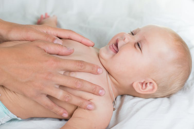 A both massages her smiling baby's stomach.