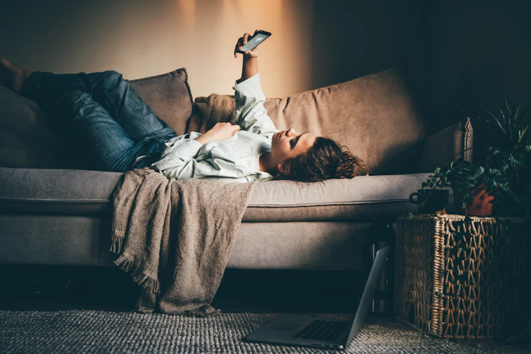 A woman lying on a sofa looking at her phone.