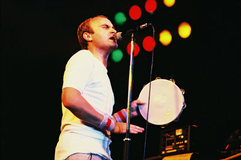 Phil Collins singing and plating a tambourine on stage.