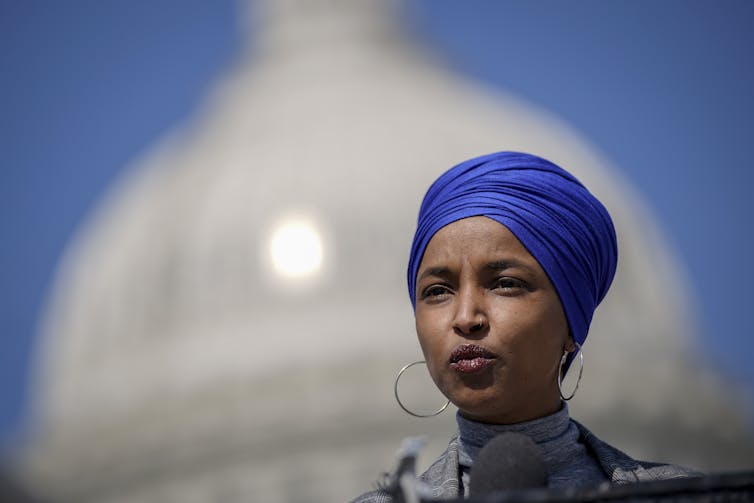 Rep. Ilhan Omar wearing a blue headcovering, in front of the U.S. Capitol.