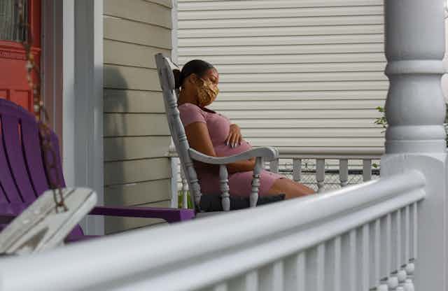 pregnant masked woman in rocking chair on porch