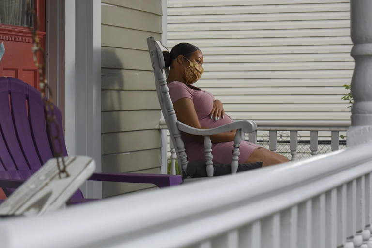 pregnant masked woman in rocking chair on porch