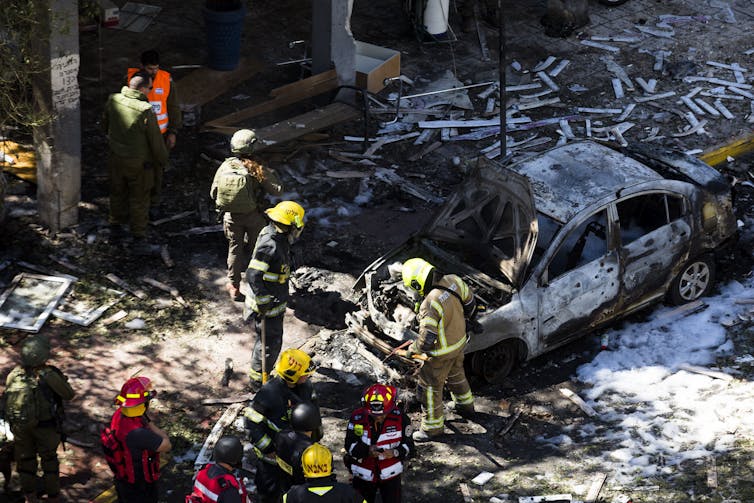 Firefighters stand around a charred car