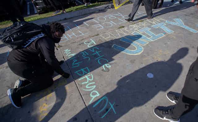 A demonstrator writes a message in chalk on the ground.