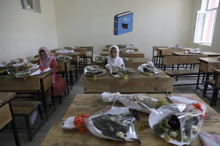 Schoolgirls sit inside a classroom with bouquets of flowers on empty desks