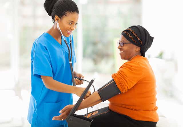 A Black female health professional taking a Black woman's blood pressure.