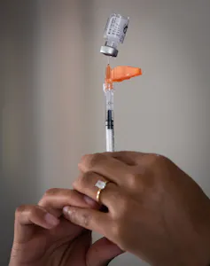 Hands holding a syringe and a vial of vaccine
