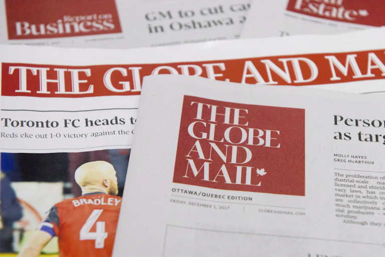 Des copies du quotidien The Globe and Mail sont étalées sur un bureau.