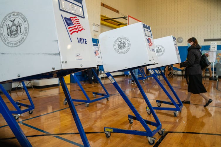 One voter standing at a white voting both that sits on blue metal legs with casters.