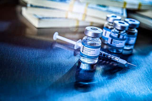 A wad of cash is stacked up behind a vial of coronavirus vaccine.