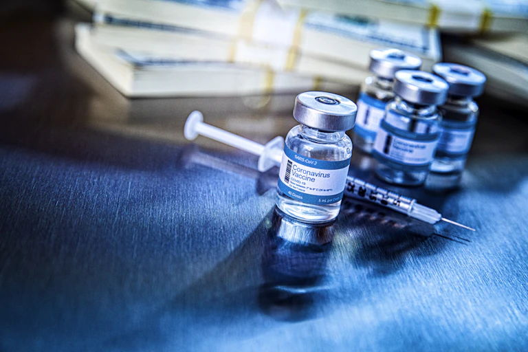 A wad of cash is stacked up behind a vial of coronavirus vaccine.