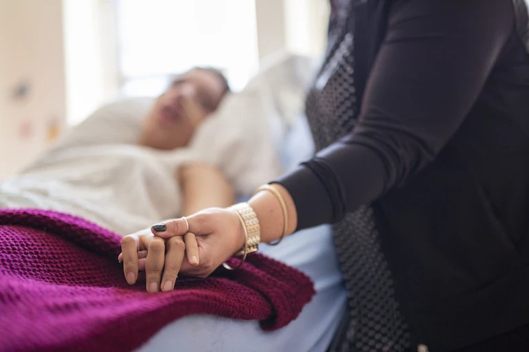 A woman holds the hand of a person in a bed.