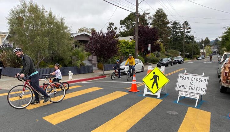 Residents ride bikes past a barrier directing traffic away from a local slow street.