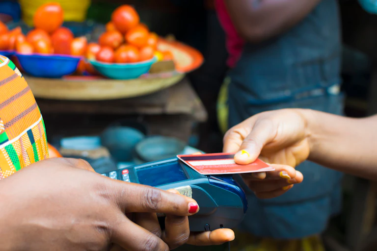Hand extending a point of sale machine to another holding an ATM card.