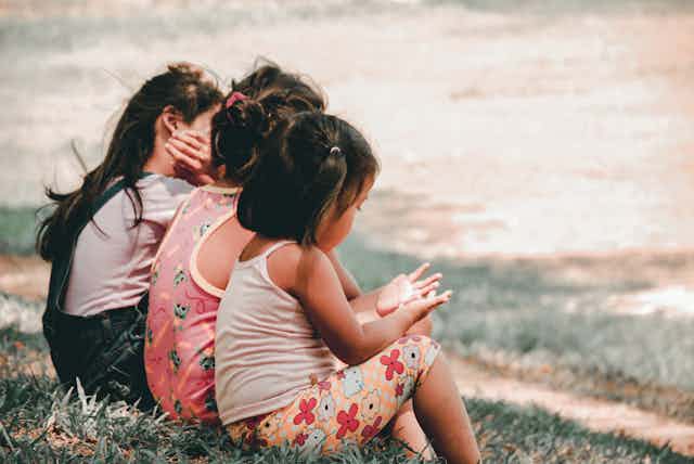 Three little girls sit side by side in a garden