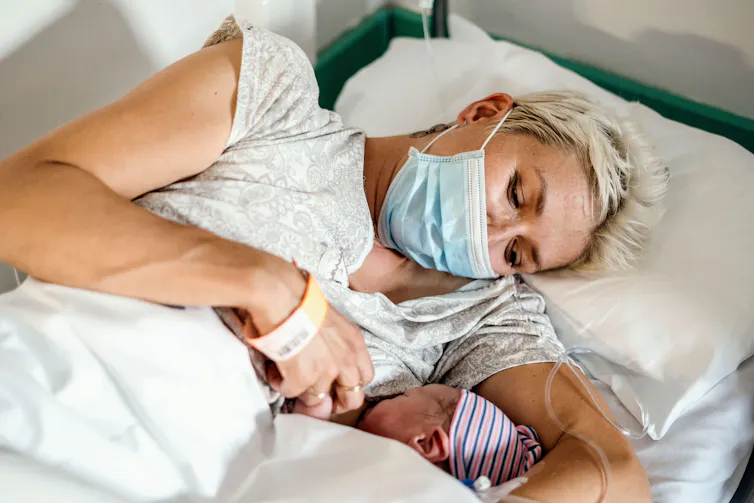 A mother breastfeeds a newborn baby in hospital, while wearing a face mask