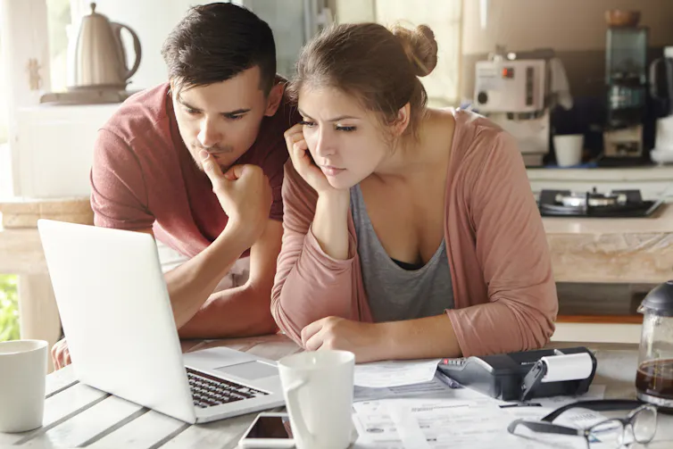 Serious man and woman sitting at kitchen table in front of open laptop computer, looking at screen