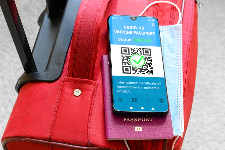 A phone showing a vaccine passport and a traditional passport on top of a travel bag
