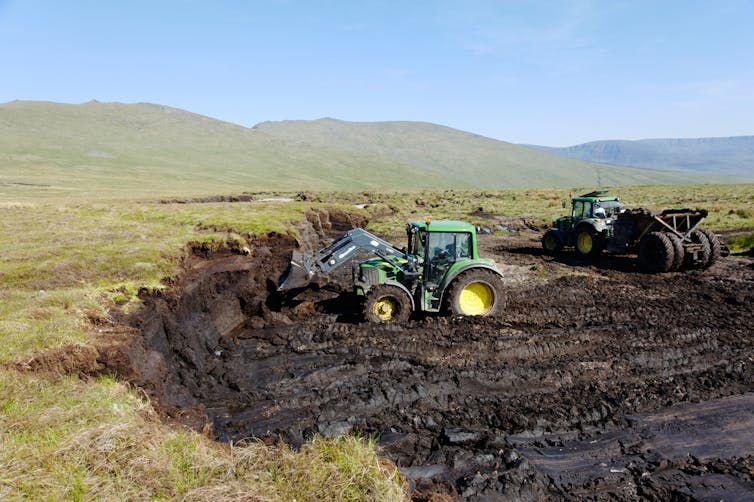 Tratores escavando turfa de dentro de uma cratera de pântano.