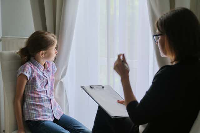 Une femme prend des notes tandis qu'une fillette regarde par la fenêtre.