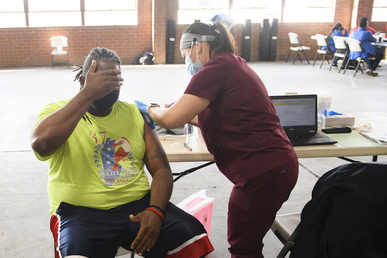 A man sitting down covers his face with his hand as he is given a COVID-19 vaccination shot.