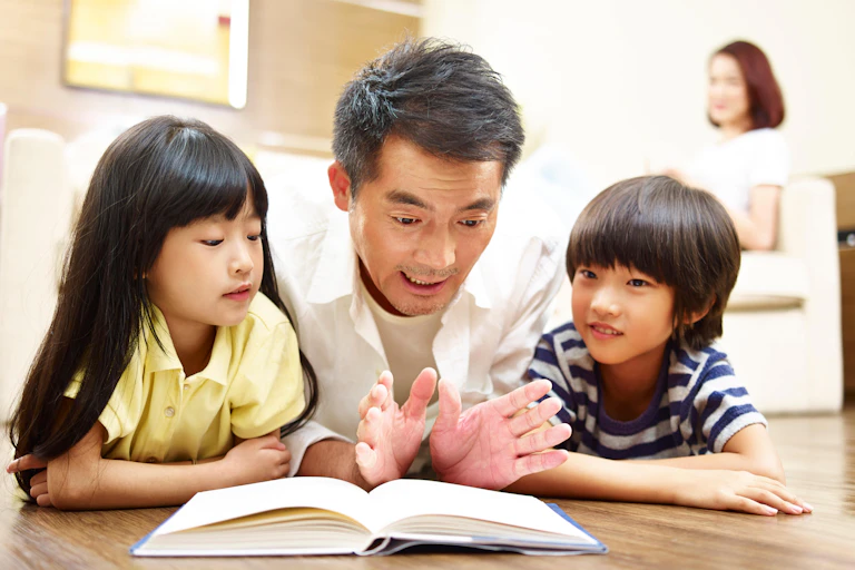 A father lies on the ground reading to his son and daughter