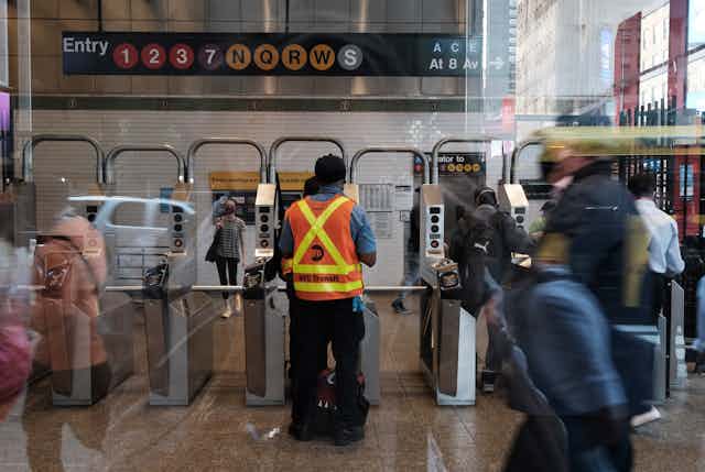 Subway worker stands near turnstiles as subway riders walk by