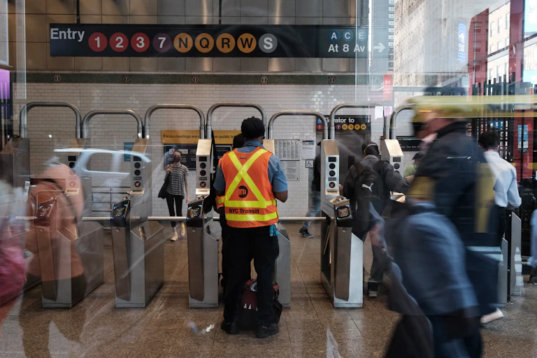 Subway worker stands near turnstiles as subway riders walk by