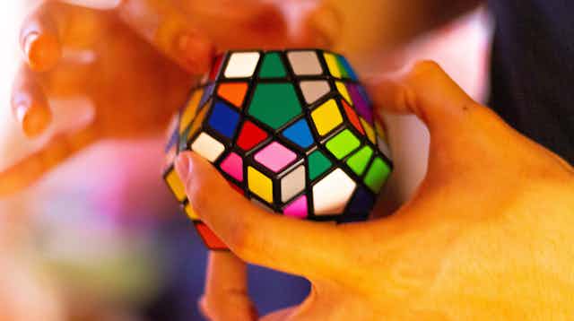 A pair of hands work a multicolored dodecahedron-shaped block puzzle