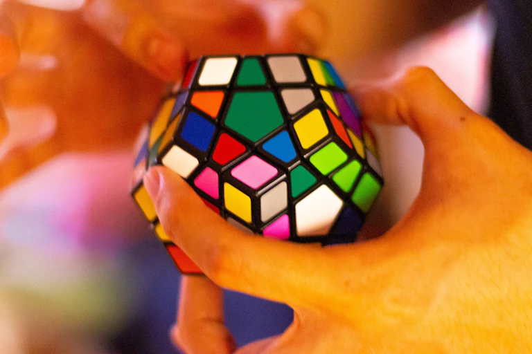 A pair of hands work a multicolored dodecahedron-shaped block puzzle