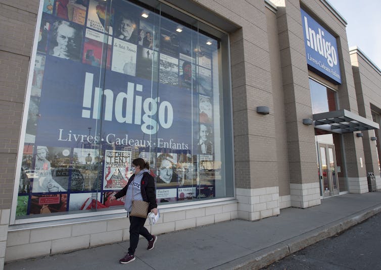 A woman in a face mask walks by an Indigo store window.