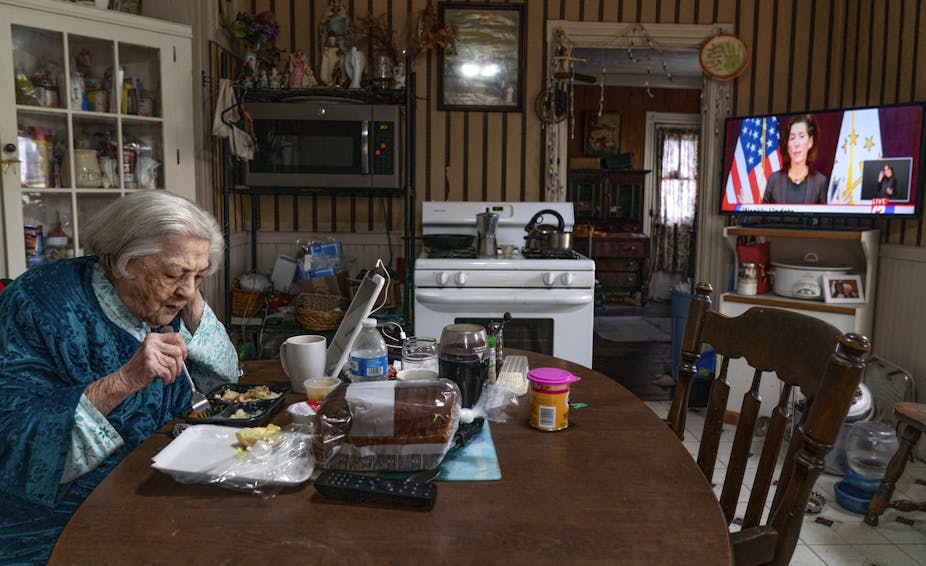 An elderly woman eats a meal by herself at her kitchen table.