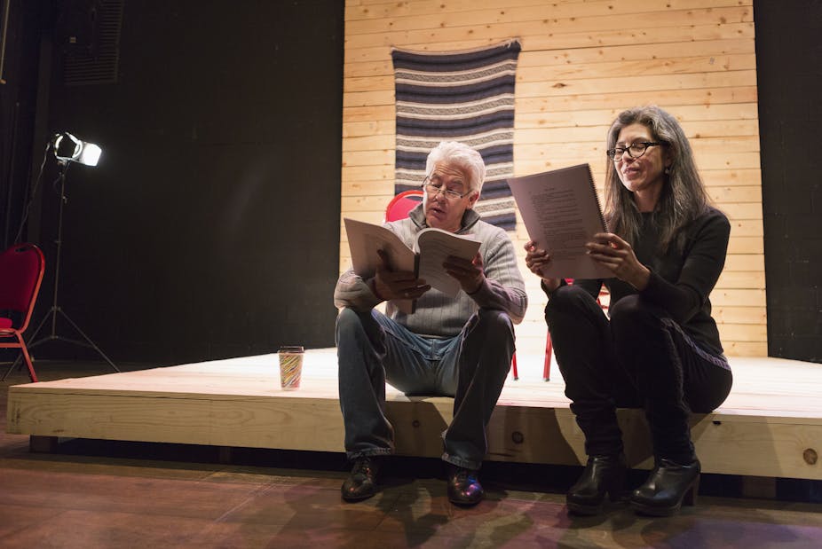 Hispanic man and woman reading scripts on theater stage.