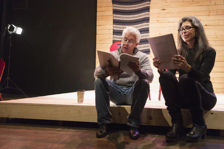 Hispanic man and woman reading scripts on theater stage.