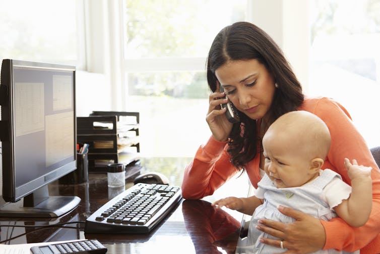 Mother on the phone holds baby on her lap as she works in her home office