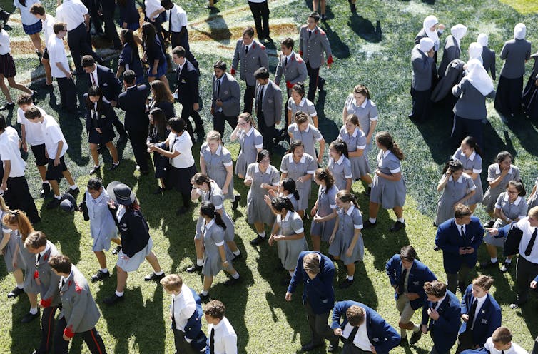 High school students in uniform gather in a park.