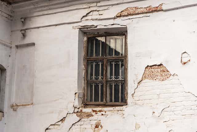 Crumbling and cracked plastering and deteriorating window on an old building