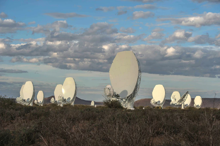A series of hexagonal objects, all of them white with grey wire-like backing, stand on a hill against a cloudy but blue sky