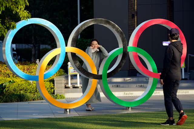 Passersby take pictures of an Olympic Rings monument displayed near the National Stadium, the main venue of the Tokyo 2020 Olympics and Paralympics