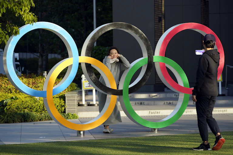 Passersby take pictures of an Olympic Rings monument displayed near the National Stadium, the main venue of the Tokyo 2020 Olympics and Paralympics