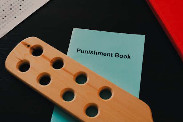 A wooden paddle and a book titled 'Punishment Book' sit on a desk.