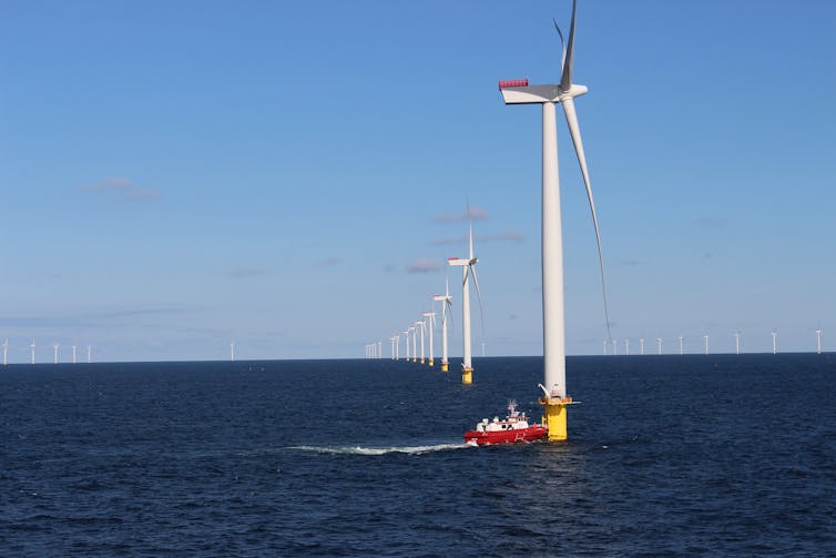 A red boat approaches a wind turbine at sea