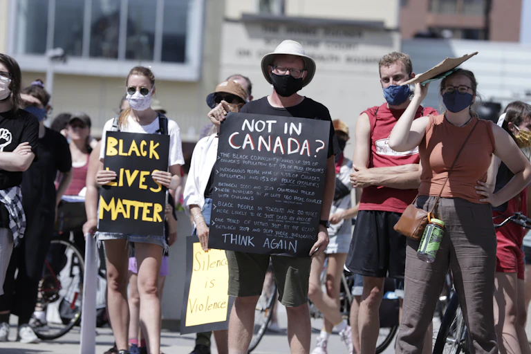 Protester holds up sign that reads 'Not in Canada? Think Again!'