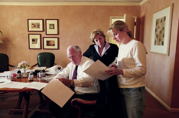 Dick, Lynne and Liz Cheney in a hotel room, looking at a document that Dick is holding.