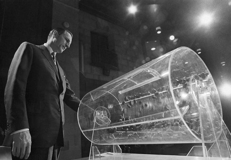 A man stands in front of a clear plastic cylinder containing tokens